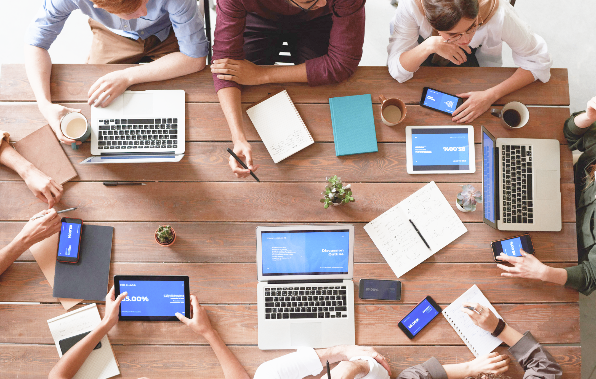 Team collaboration with laptops and devices around a wooden table